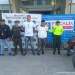 Se aprecia a los dos capturados junto a un investigador del CTI y dos uniformados de la Policía Nacional. En la parte posterior los banners que identifican a la Policía Nacional y a Fiscalía General de la Nación