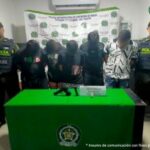 En la fotografía aparecen cinco hombres que se encuentran de pie con las cabezas agachadas, custodiados por dos agentes de la Policía Nacional. Delante de ellos hay una mesa que tiene en la superficie el arma incautada y un reloj.