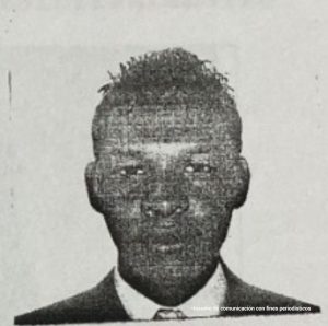 En la fotografía a blanco y negro está el rostro de un hombre de ojos pequeños, nariz y labios gruesos. Se encuentra vestido con saco y corbata.