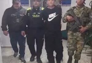 En la foto se aprecia en acción de caminata, por pasillo, a Yojan Abel Rodríguez Duarte. Viste con camiseta de manga corta negra con estampado blanco a la altura del pecho con la palabra ‘Nike’ y el símbolo correspondiente; pantalón y zapatos negros. Al lado derecho de él hay un servidor del CTI de la Fiscalía y un uniformado de la Policía Nacional. Al lado izquierdo un uniformado del Ejército.