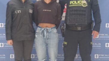 En la fotografía aparece la capturada junto a una servidora del CTI y un agente de la Policía Nacional. En la parte superior está un banner de la Fiscalía General