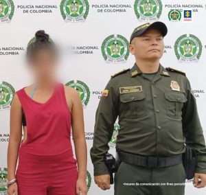 en la imagen se ve una mujer detenida bajo custodia de un uniformado de la Policía Nacional. Detrás suyo un backing institucional.