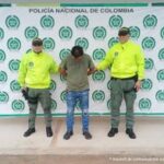 El capturado aparece con sus manos esposadas a la espalda, con la cara agachada y custodiado por dos uniformados de la policía nacional.