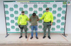 El capturado aparece con sus manos esposadas a la espalda, con la cara agachada y custodiado por dos uniformados de la policía nacional.