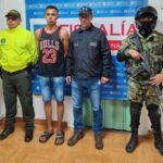 En la imagen se ve una persona de espaladas, detenida, bajo custodia de dos integrantes de la Policía Naciona