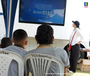 En la foto se aprecia a estudiantes observando un video en una pantalla en la que se aprecia una de las líneas de atención: la 122 para denunciar cualquier delito la Fiscalía General de la Nación.