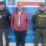 capturados de frente custodiados por investigador del CTI de la Fiscalía y Policía. Detrás banner de Fiscalía.