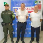 Se visualiza a los dos capturados junto a un uniformado de la Policía Nacional. Detrás se encuentra el banner de la Fiscalía General de la Nación