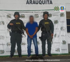 Se visualiza al capturado con el rostro difuminado junto a dos uniformados de la Policía Nacional. Detrás de ellos el banner que identifica a la Policía en Arauca.