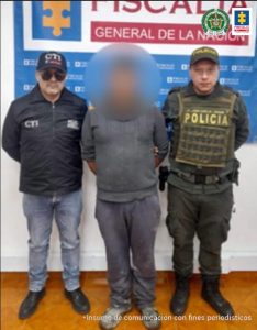 En la fotografía aparece el capturado junto a un servidor del CTI y un agente de la Policía Nacional. En la parte superior está un banner de la Fiscalía General de la Nación