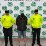 El capturado está de frente a la cámara con la cara agachada, viste una chaqueta oscura y tiene un short de jean, custodiado por dos uniformados de la Policía Nacional.