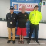 Se visualiza al capturado con el rostro difuminado junto a un investigador del CTI y un integrante de la Sijin. Detrás el banner que identifica a la Fiscalía General de la Nación