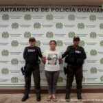 capturada de frente custodiada por dos policías. Detrás banner de la Policía Nacional.