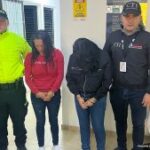 Se observan dos mujeres capturadas al centro. A un costado un funcionario del Cuerpo Técnico de Investigación CTI y al otro lado uno de la Policía Nacional. Atrás las banderas de la Fiscalía general de la Nación y la de ColombiaPIE DE FOTO: Lady Johanna Vargas Rojas y Diana Marcela Ruiz Rojas fueron privadas de la libertad