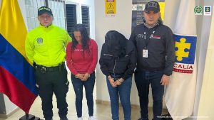Se observan dos mujeres capturadas al centro. A un costado un funcionario del Cuerpo Técnico de Investigación CTI y al otro lado uno de la Policía Nacional. Atrás las banderas de la Fiscalía general de la Nación y la de ColombiaPIE DE FOTO: Lady Johanna Vargas Rojas y Diana Marcela Ruiz Rojas fueron privadas de la libertad
