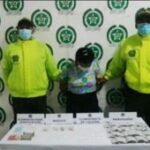 La mujer aparece en medio de dos uniformados de la policía y en una mesa los elementos materiales de prueba tales como cocaína, marihuana y base de coca.