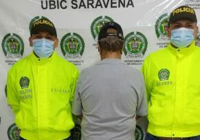 Se visualiza al capturado de espaldas junto a dos uniformados de la Policía Nacional. Detrás el banner que identifica a la Policía Nacional en Saravena (Arauca)