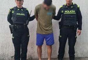 El capturado está con su rostro agachado, y sujetado por dos uniformados de la policía nacional.