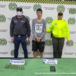 En la fotografía se aprecia de pie, con los brazos adelante y esposado a Cristhian David Zapata. Viste buso de manga larga de color gris con estampado blanco a la altura del pecho y bermuda negra. Al lado derecho de él hay un servidor del CTI de la Fiscalía y a la derecha un uniformado de la Policía Nacional. Delante de ellos, sobre una superficie verde hay munición y un teléfono celular. Asimismo, hay dos letreros que dicen: ‘Munición’. Y ‘Celular incautado’. Detrás de ellos hay un pendón institucional de la Policía.