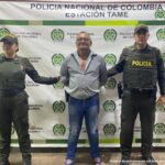 Se visualiza al capturado junto a dos uniformados de la Policía Nacional. Detrás el banner que identifica a la Estación de Policía de Tame (Arauca)