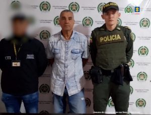 En la fotografía se aprecia de pie y con los brazos atrás a Rubén Darío Yepes Rendón. Viste camisa de manga corta de botones y dos bolsillos en la parte superior, de color azul claro; jean azul. A sus extremos hay uniformados de la Policía Nacional. Detrás de ellos hay un pendón institucional de la Policía.