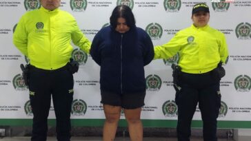 La mujer capturada está esposada con sus manos a la espalda, está vestida con ropa color negro y la custodian dos miembros de la Policía Nacional
