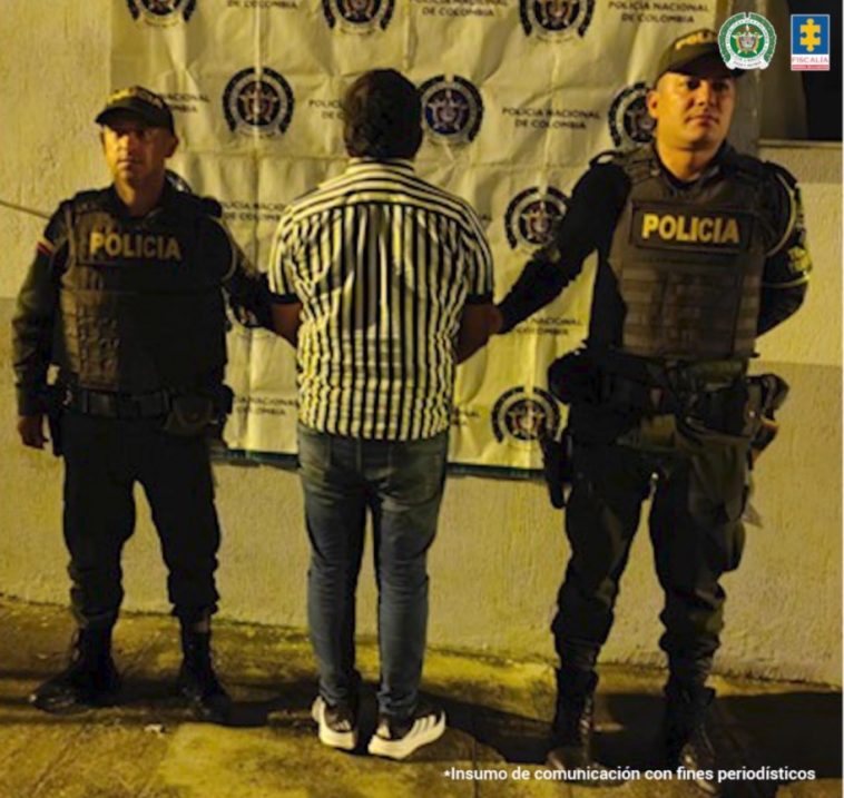 En la imagen se ve una persona detenida de espaldas, bajo custodia de la Policía Nacional.