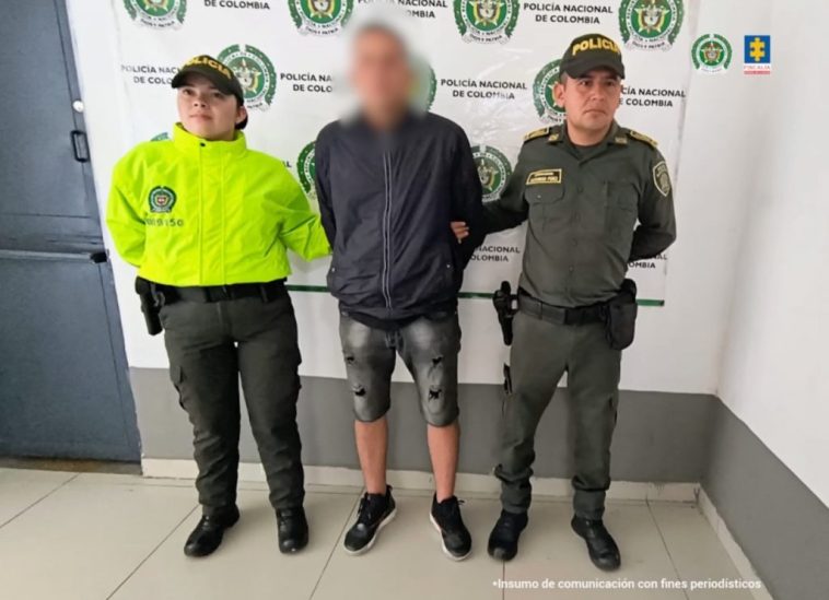 En la imagen podemos ver a una persona detenida de espaldas, bajo la custodia de dos miembros de la Policía Nacional.  Detrás de él está el apoyo institucional.