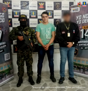 El capturado es visto junto a un uniformado del Ejército Nacional y un investigador del CTI.  Detrás de ellos las pancartas que identifican al Ejército Nacional.