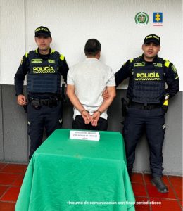 Un capturado se ve de espaldas al frente de una mesa con un mantel verde y el aviso, acto sexual abusivo con un menor de 14 años, y a cada lado del capturado un oficial de la Policía Nacional uniformado.