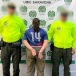 Se visualiza a la capturada de espaldas junto a dos uniformados de la Policía Nacional. Detrás el banner institucional de la Policía Nacional