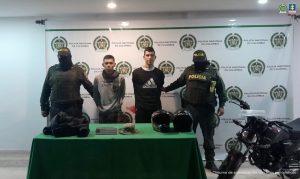 Los capturados se encuentran en custodia por dos uniformados de la Policía Nacional. En la foto se observa parte de los elementos incautados como la motocicleta y otros objetos . Detrás se observa un backing de la Policía.