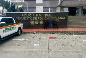 La procesada se encuentra en custodia por dos uniformados de la Policía Nacional. En la foto se observa parte de la munición incautada. Detrás se observa un backing de la Policía.