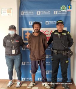 En la fotografía aparece el capturado junto a un servidor del CTI y un agente de la Policía Nacional. En la parte superior está un banner de la Fiscalía General