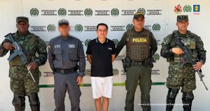 en la imagen un hombre (de camiseta negra con pantaloneta blanca) detenido bajo custodia del Ejército y el CTI.