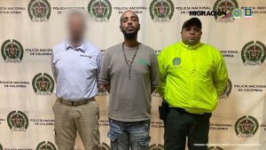 En la imagen está el procesado con un servidor de la Policía Nacional y uno de Migración Colombia, con el rostro distorsionado, a los lados.