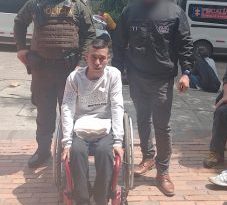 En la fotografía, tomada en exteriores, se aprecia a Miller Steven Cardona Agudelo sentado en una silla de ruedas. Viste Buso de color gris claro, pantalón negro y zapatillas blancas con negro. Sobre sus piernas tiene una prensa blanca doblada. A su izquierda hay un servidor del CTI de la Fiscalía y a su derecha un uniformado de la Policía Nacional. Detrás de ellos se ven dos vehículos institucionales de la Fiscalía.