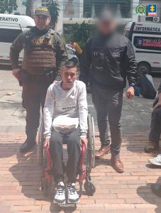 En la fotografía, tomada en exteriores, se aprecia a Miller Steven Cardona Agudelo sentado en una silla de ruedas. Viste Buso de color gris claro, pantalón negro y zapatillas blancas con negro. Sobre sus piernas tiene una prensa blanca doblada. A su izquierda hay un servidor del CTI de la Fiscalía y a su derecha un uniformado de la Policía Nacional. Detrás de ellos se ven dos vehículos institucionales de la Fiscalía.