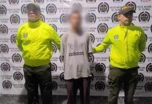 en la imagen se ve una persona detenida bajo custodia de dos integrantes de la Policía Nacional.