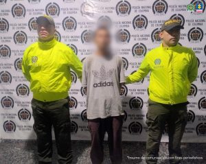 en la imagen se ve una persona detenida bajo custodia de dos integrantes de la Policía Nacional.