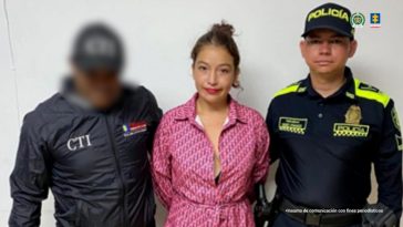 En la fotografía se aprecia de pie y con los brazos atrás a María de Los Ángeles Vélez Castillo. Tiene prenda tipo vestido de color rojo estampado, así como zapatilla negras con fucsia. Al lado derecho de ella hay un servidor del CTI de la Fiscalía y al lado izquierdo un uniformado de la Policía Nacional.