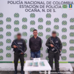 Se visualiza al capturado junto a dos uniformados de la Policía Nacional. Frente a ellos en una mesa el dinero exigido. Detrás de ellos el banner que identifica a la Policía Nacional.