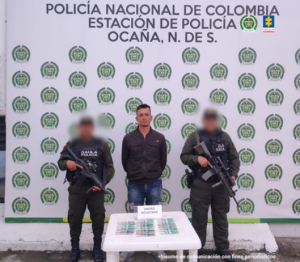 Se visualiza al capturado junto a dos uniformados de la Policía Nacional. Frente a ellos en una mesa el dinero exigido. Detrás de ellos el banner que identifica a la Policía Nacional.