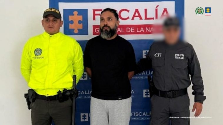 Se observa al capturado de frente, a un costado un funcionario del Cuerpo Técnico de Investigación CTI y al otro uno de Policía Nacional. Atrás un pendón de Fiscalía General de la Nación