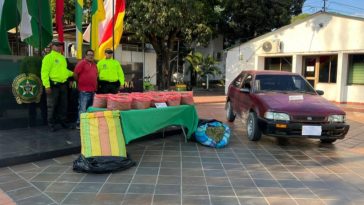 Se observa al capturado custodiado por dos uniformados de la Policía Nacional. En la imágen se puede apreciar una mesa con el estupefaciente incautado y el vehículo.