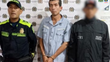 En la fotografía se aprecia de pie, con los brazos adelante y esposado a César Piter Vásquez Erazo. Viste camisa de manga corta, de color azul claro; pantalón de color mostaza, zapatillas negras con zuela blanca. Al lado izquierdo hay un servidor del CTI de la Fiscalía y al lado derecho hay un uniformado de la Policía Nacional. Detrás de ellos hay un pendón institucional de la Policía.