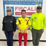 capturado de frente custodiado por un investigador del CTI de la Fiscalía y un policía. Detrás banner de la Fiscalía.