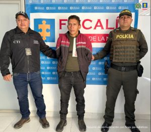 En la fotografía se aprecia de pie y con los brazos atrás a  Jesús Bernardo Mamián. Viste con camiseta de color verde oscuro y sobre ella una chaquela que en la parte superior es de color vinotinto y en la parte de abajo verde oscuro; asimismo, pantalón y zapatos negros. A su derecha hay un servidor del CTI de la Fiscalía. A su izquierda un uniformado de la Policía Nacional. Detrás de ellos hay un pendón institucional de la Fiscalía.