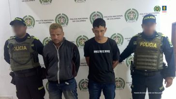 En la fotografía aparecen dos hombres de pie, con los brazos atrás esposados, vestidos con camisetas negras y jean azul, custodiados por dos uniformados de la Policía Nacional. Detrás de ellos hay un pendón de la Policía Nacional.