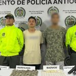 En el centro de la imagen aparece el capturado junto a otra persona con el rostro distorsionado. A cada extremo de la foto aparecen dos miembros de la Policía. En el fondo hay un banner de la Policía.